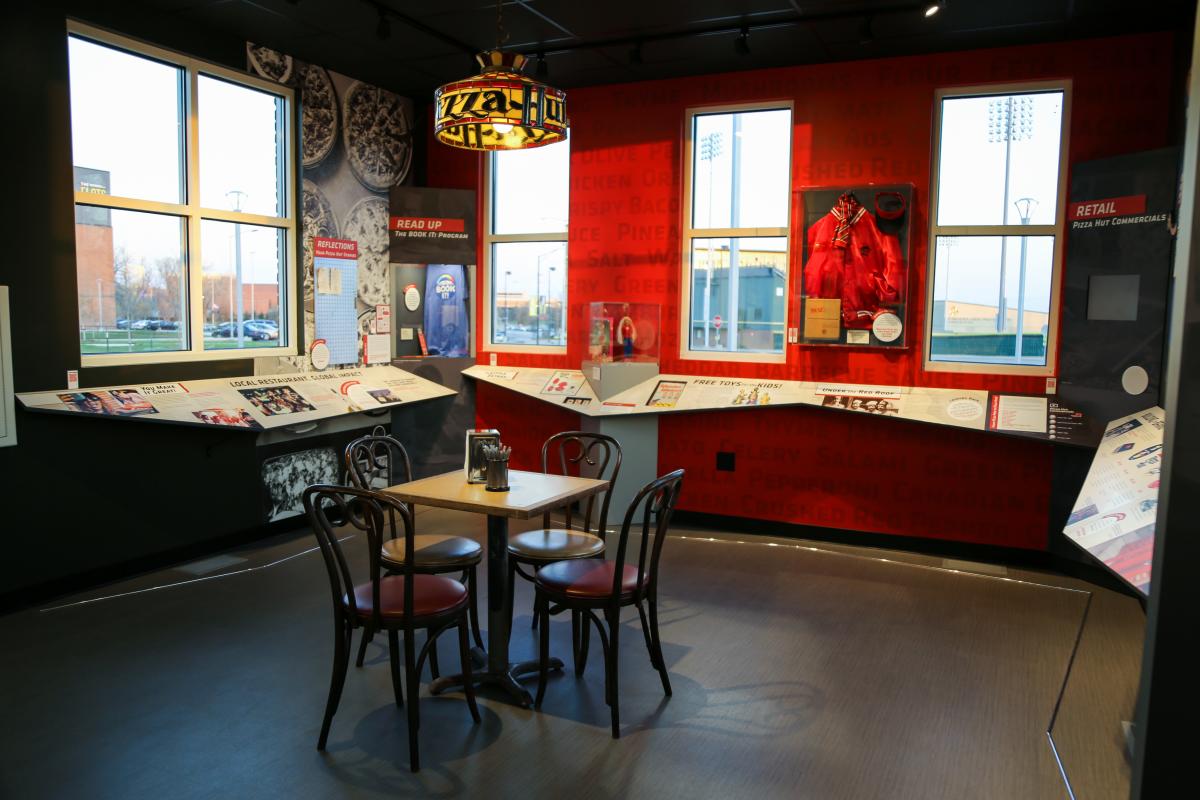 The interior of the Pizza Hut museum displays memorabilia and an old restaurant table, chair and lap
