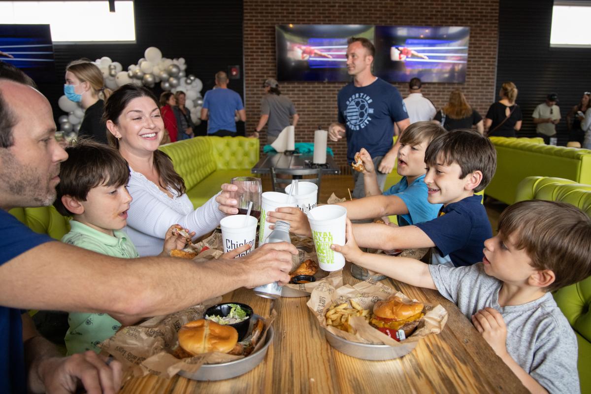 A family of a mom, dad and four boys toast at a table at Chicken N Pickle
