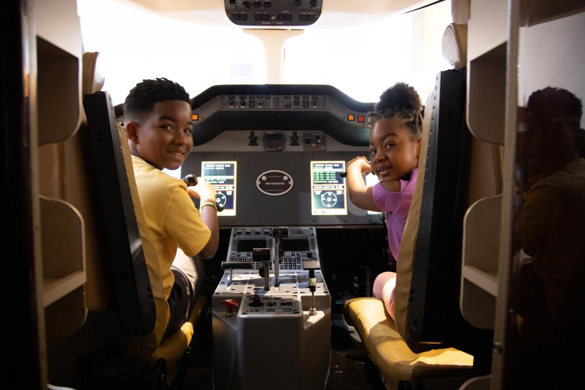 A young black boy and his sister play on the flight simulator at Exploration Place