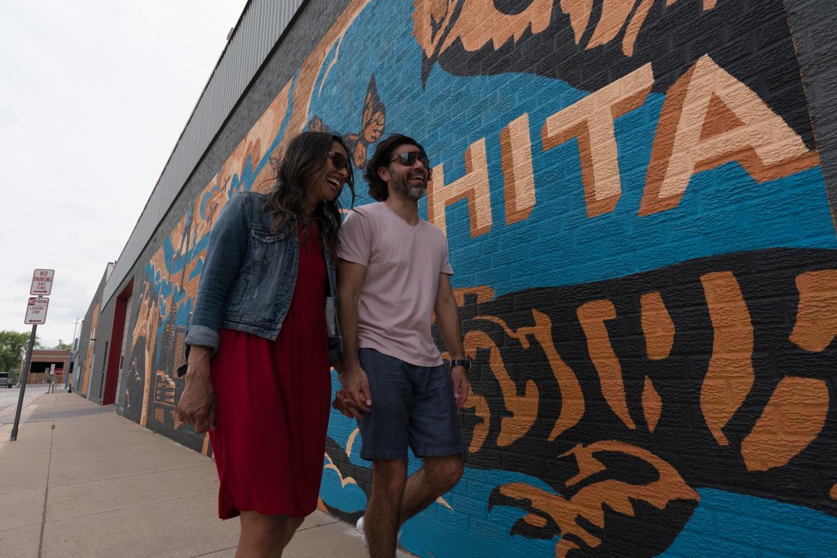A couple walks down the street past a mural on a building in Wichita