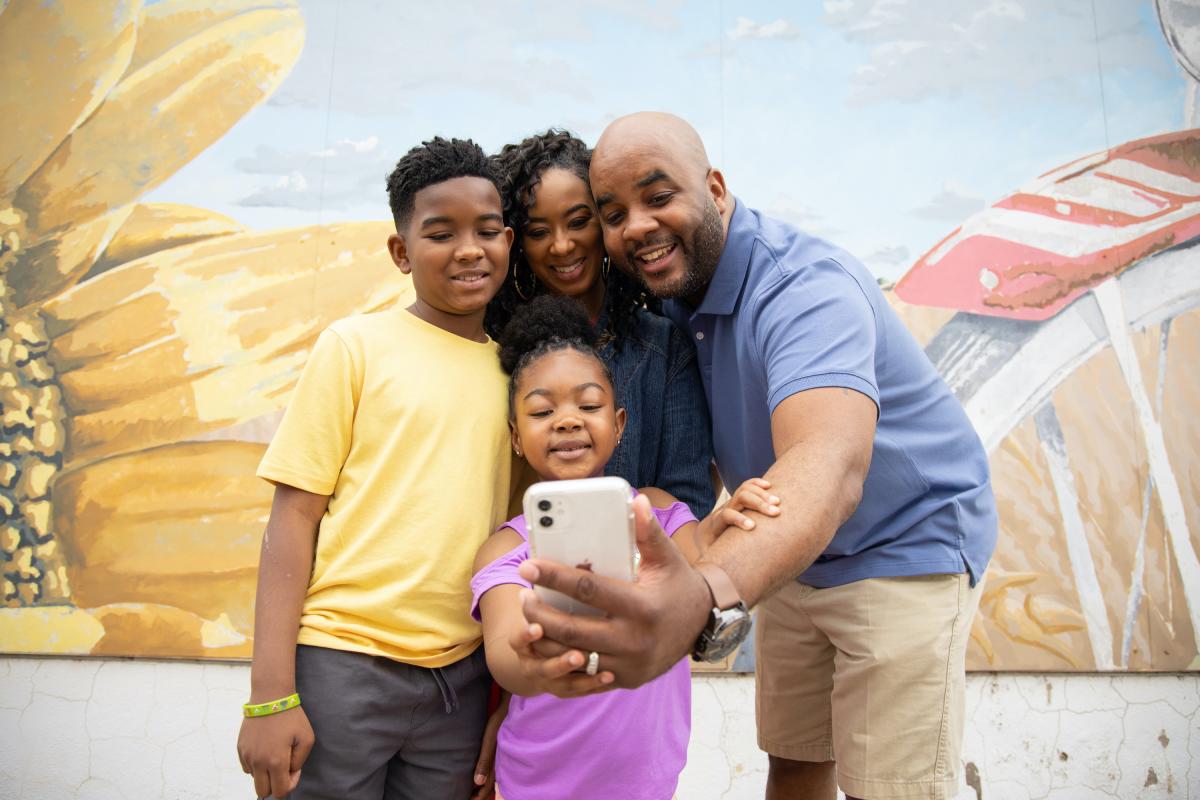A mother, father, son and daughter take a selfie together in front of a public mural in Wichita, KS