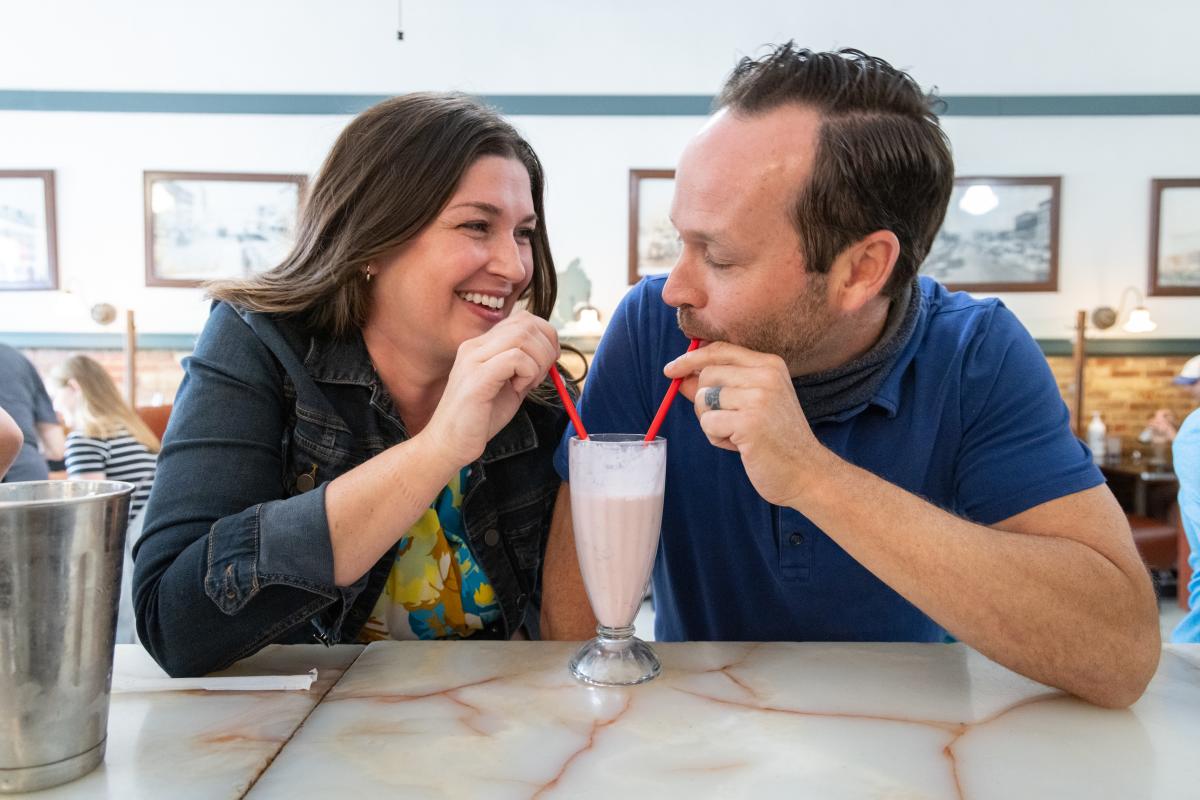 A man and woman sip from the same milkshake at Old Mill Tasty Shop