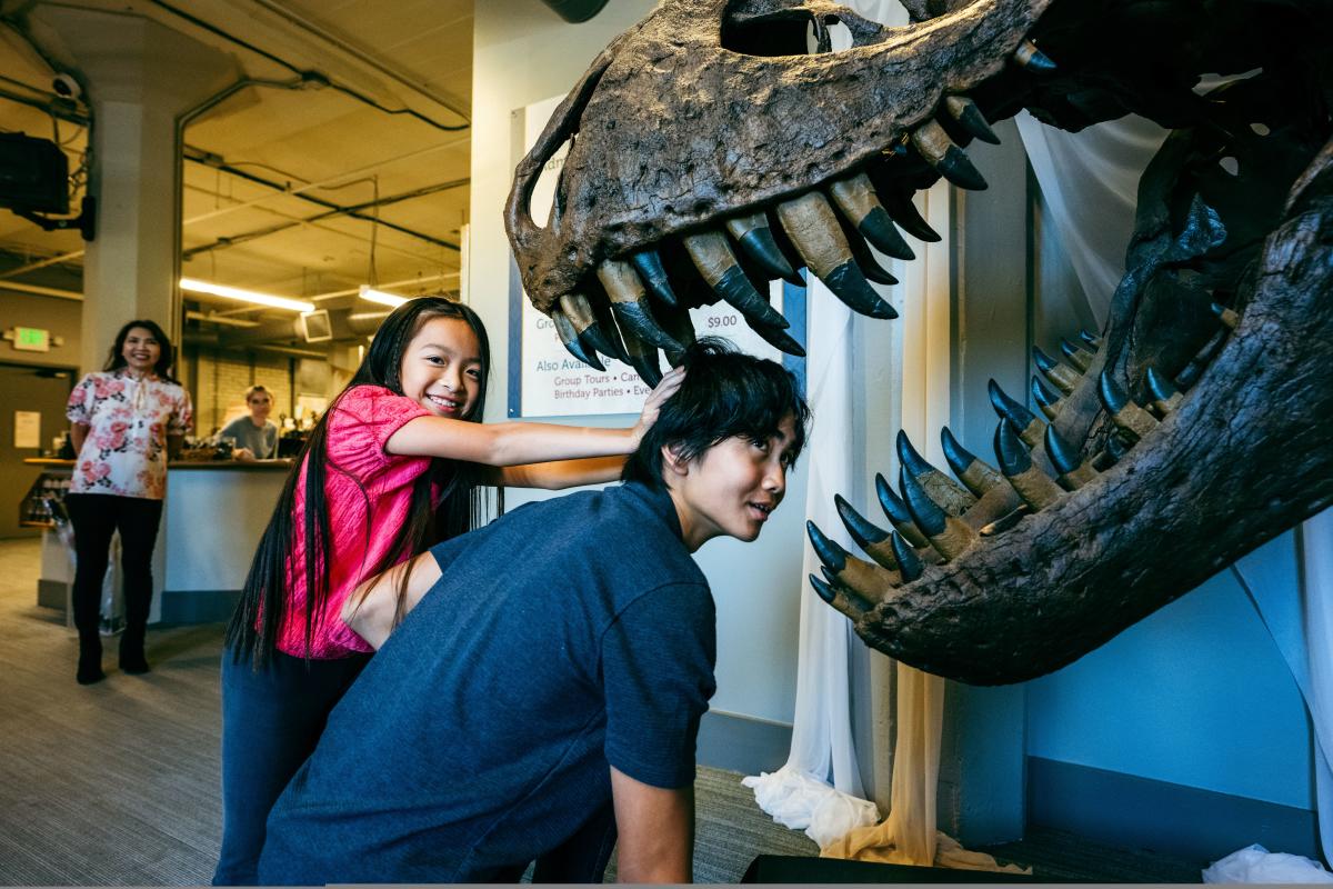 A girl poses with her brother near the mouth of a dinosaur skeleton at Museum of World Treasures.