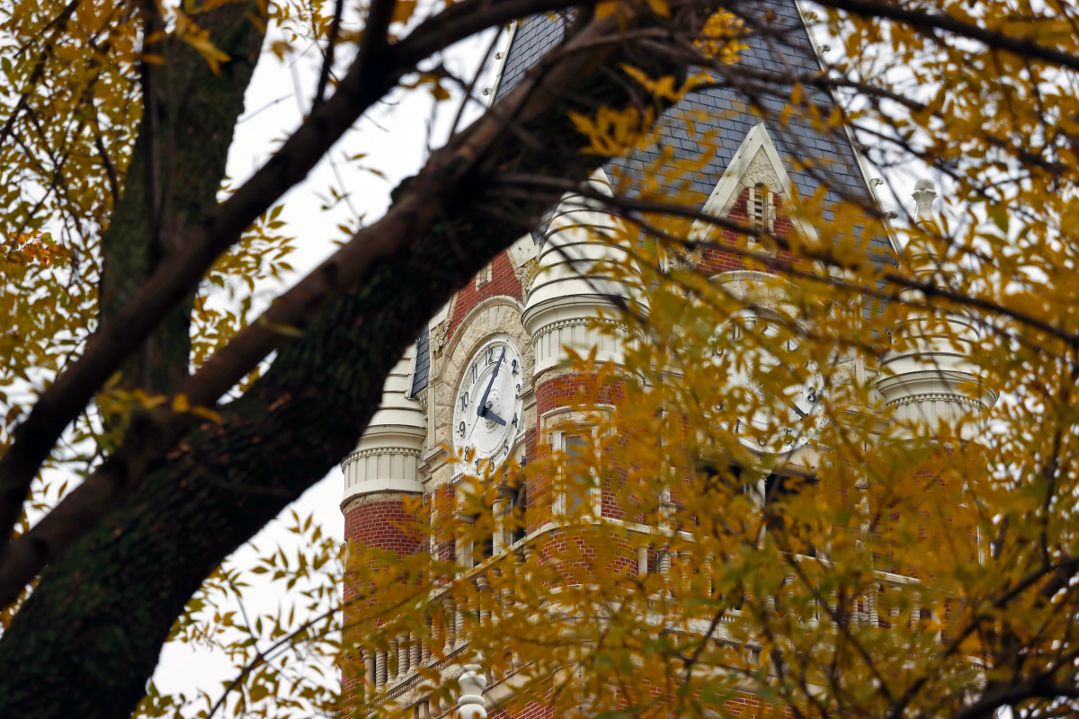 The clock tower at Friends University peeks through orange leaves on a tree