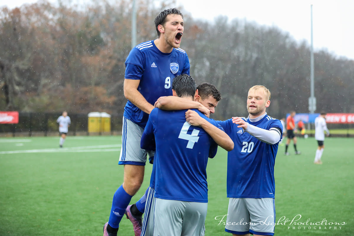 Three college male soccer players celebrate on the field during a game at the NAIA Championship