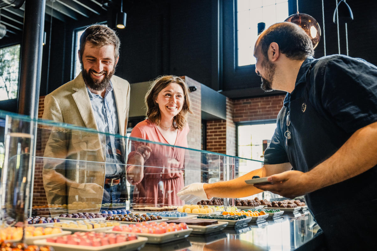A man and woman smile at and employee at Cocoa Dolce while he helps them choose chocolates from the display case.