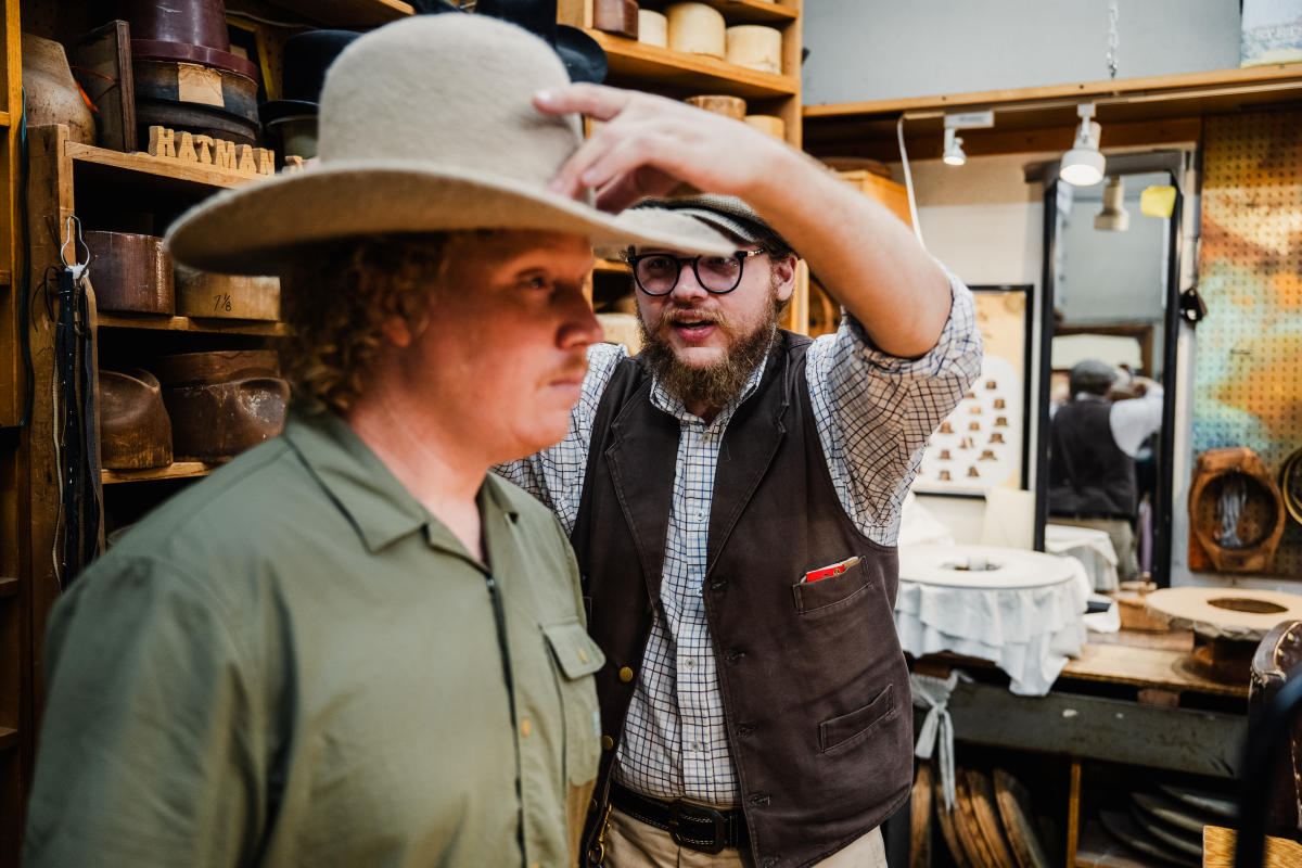 A staff member at Hatman Jack's fits a male customer for a hat.