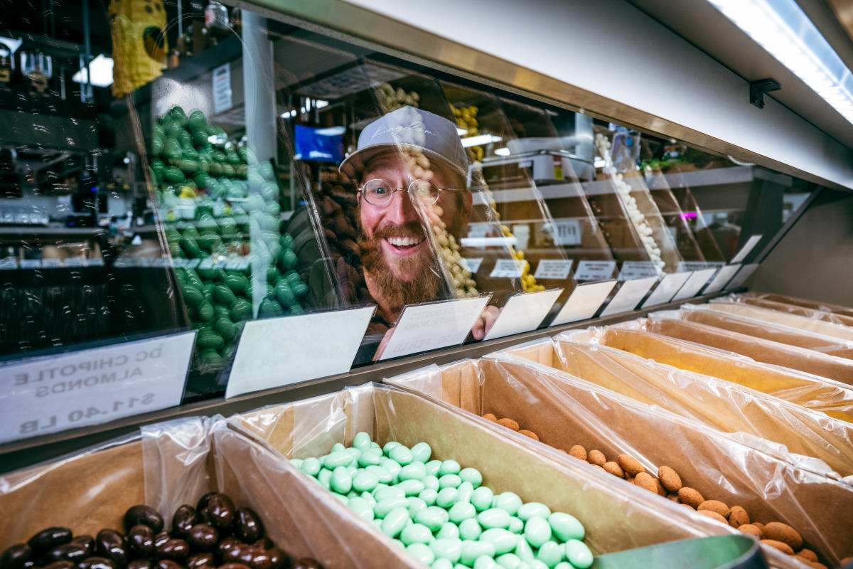 A man smiles while looking through a glass display at candy at the Nifty Nut House.