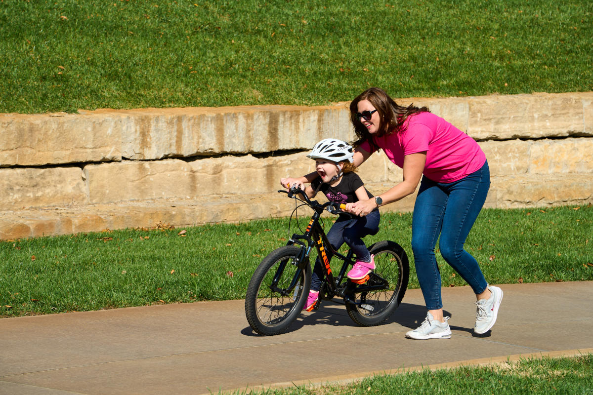 A mom guides her daughter on a rented scooter near the Arkansas River