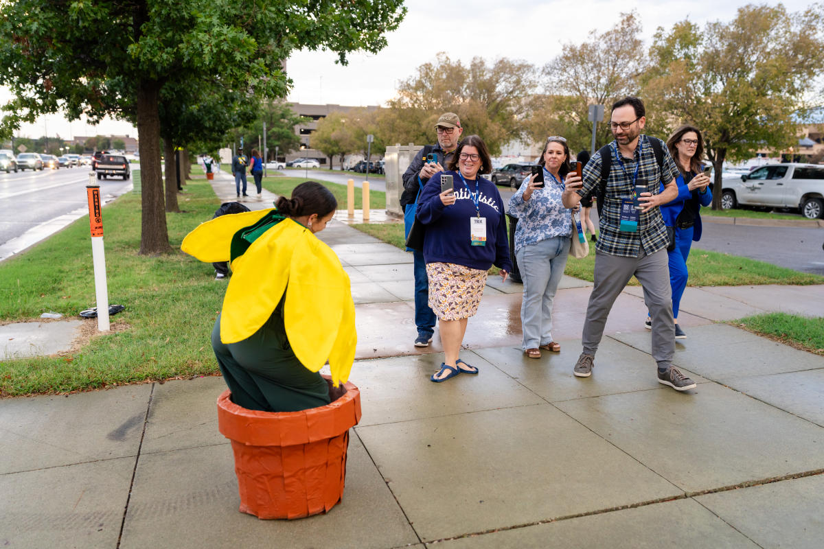 A woman performs as a potted flower while TBEX attendees walk to a VIP event in Wichita.