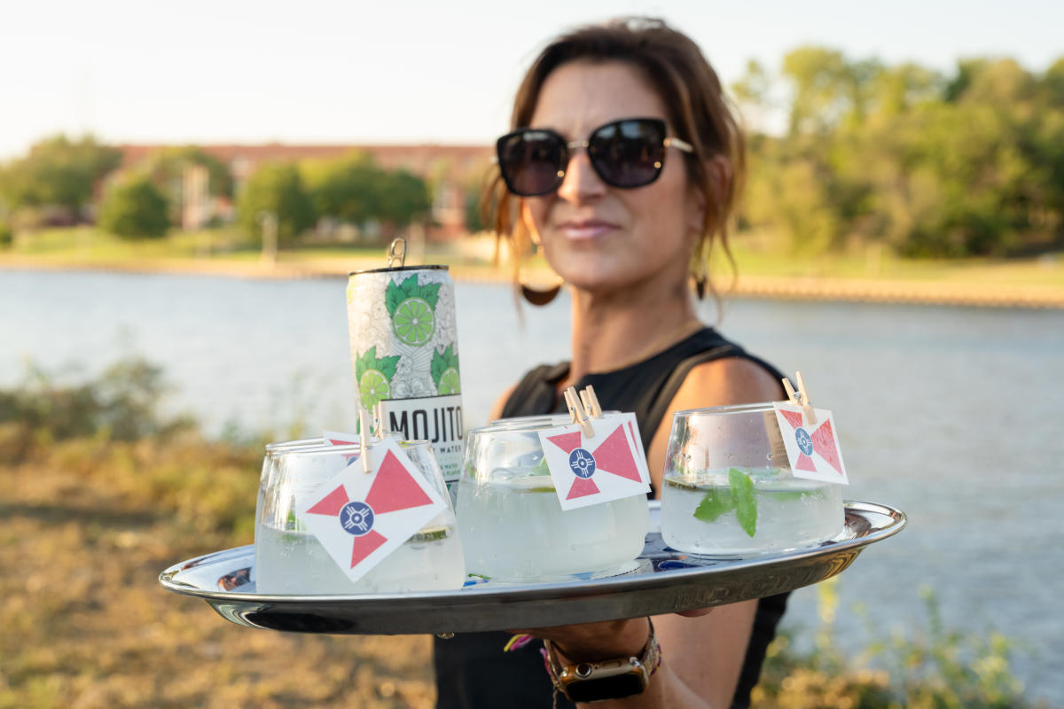 A woman serves cocktails on a tray with Wichita Flags to TBEX attendees.