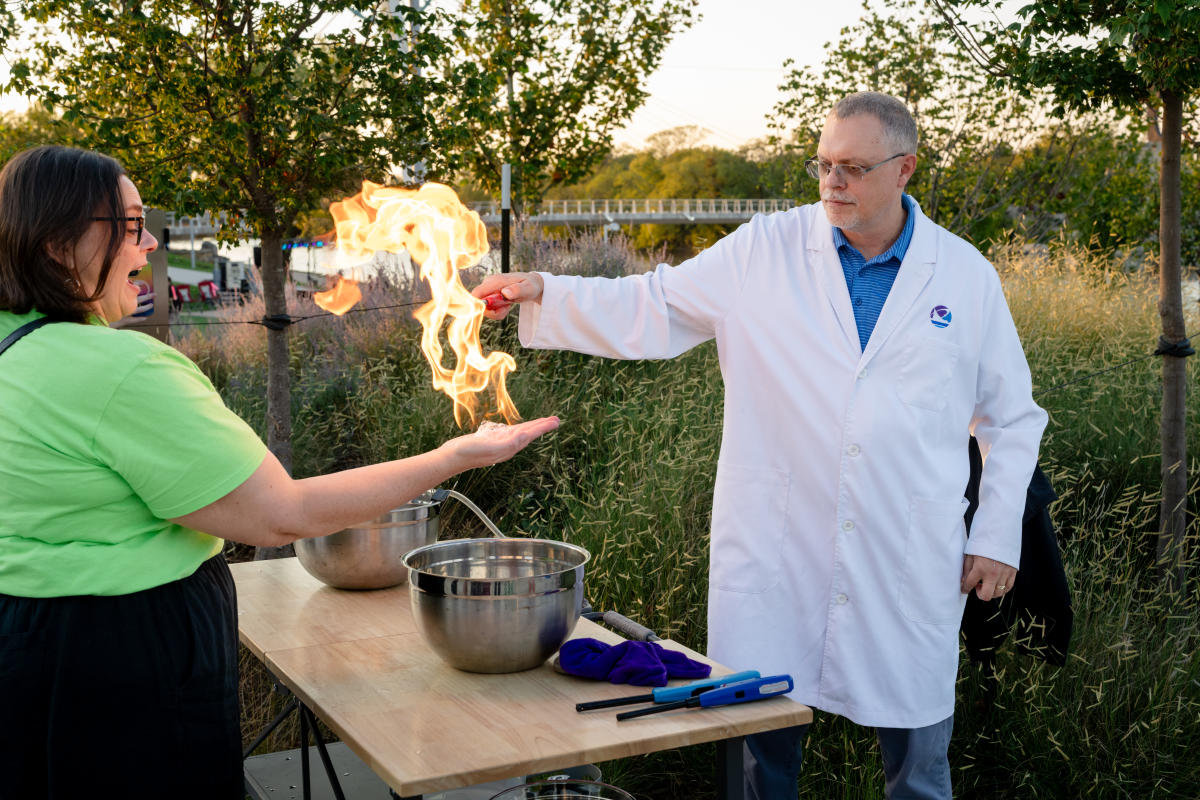 A woman is delighted as fire ignites in her hand at a STEM demonstration at Exploration Place