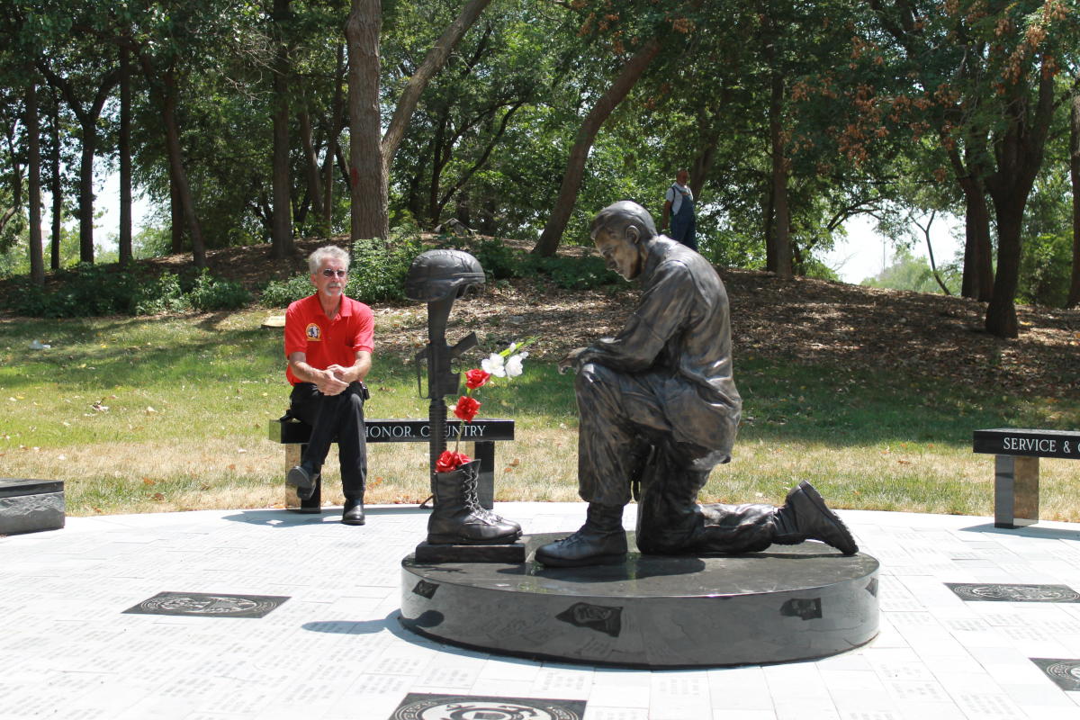 A man pays his respects while sitting on a bench near a statue at Wichita's Veteran's Memorial Park