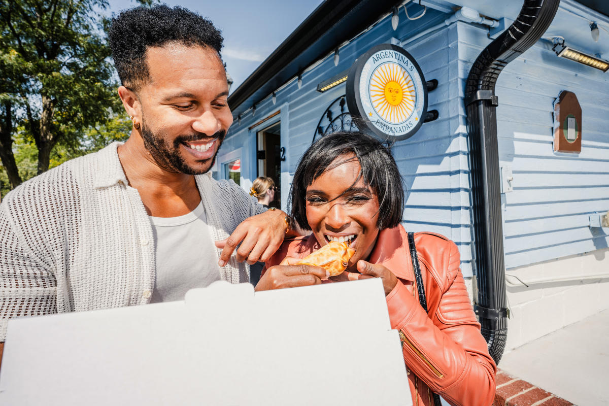 A woman gets ready to bite into a fresh empanada at Argentina's Empanadas while the man with her smiles.