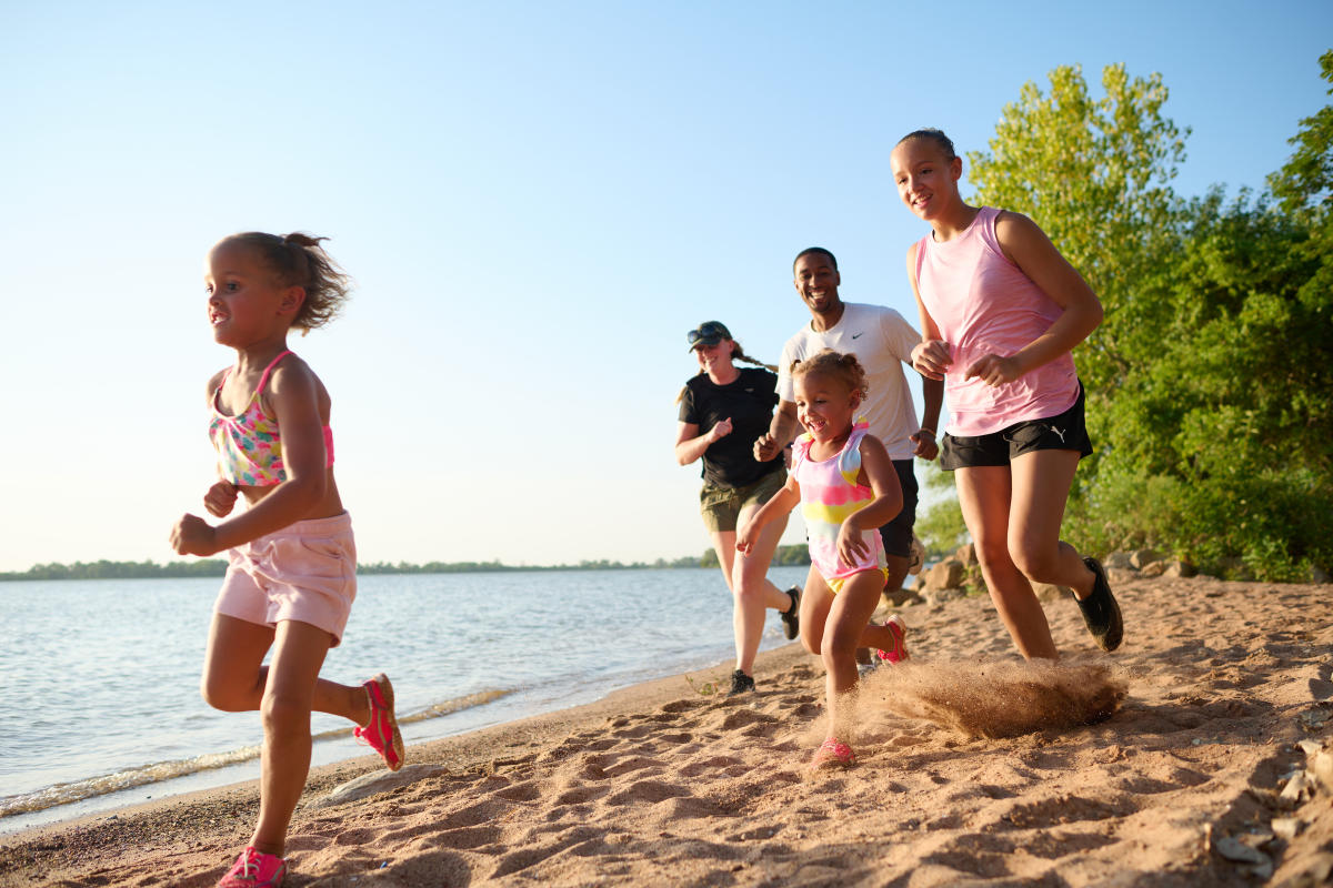 A young family runs along the beach on the lake at Cheney State Park