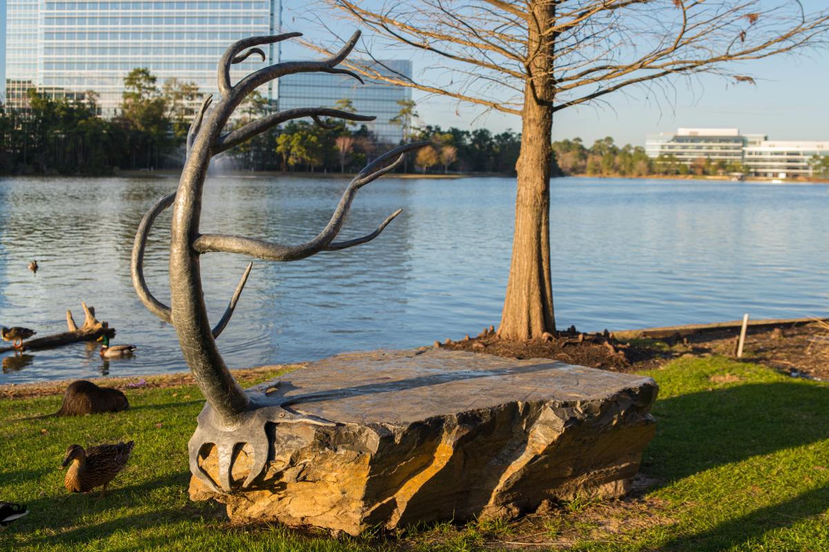 Art Bench with an iron tree sitting atop a rock base near a lake