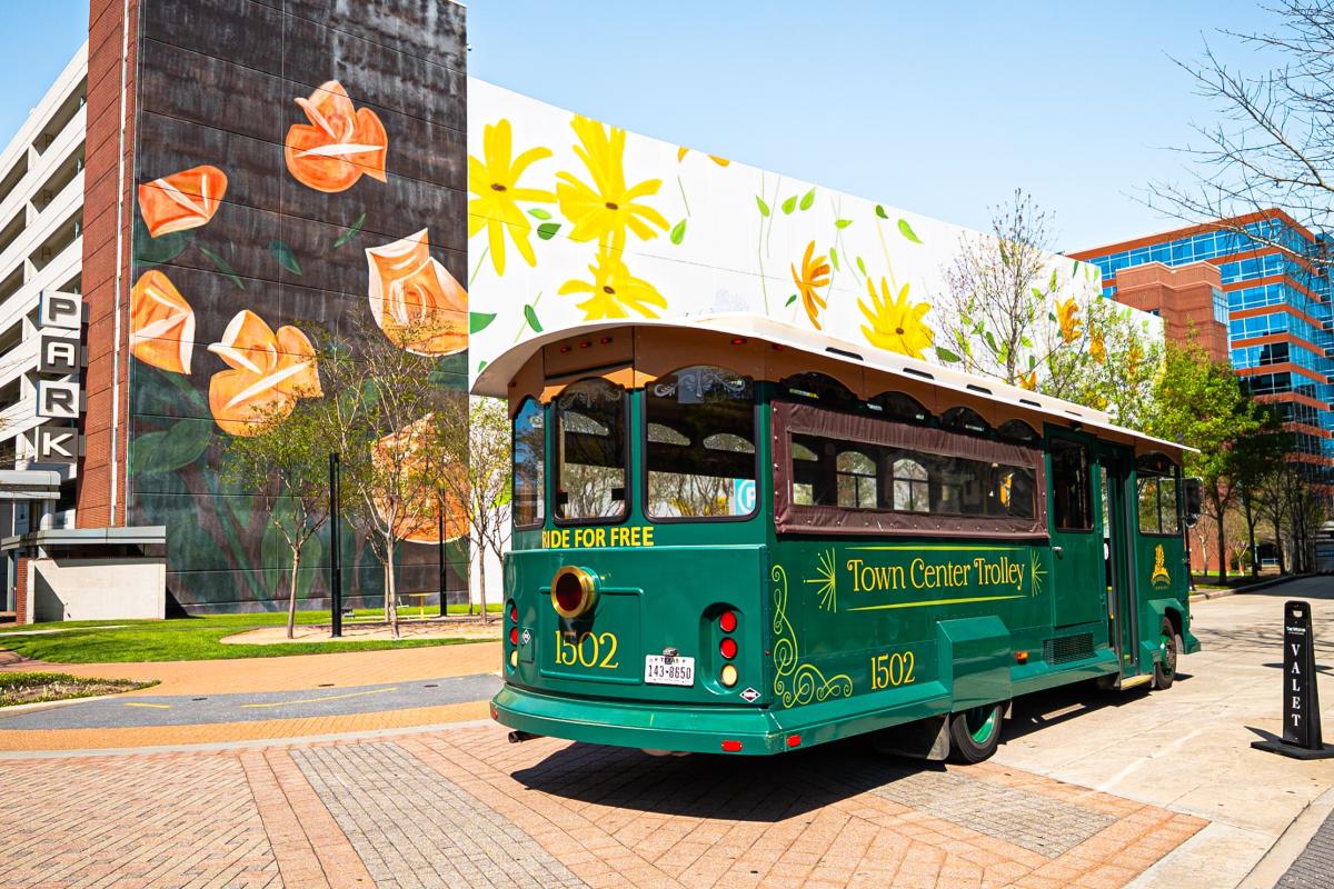 A bright green trolley bus drives past The Westin in Waterway Square. Behind it is a large mural of yellow and orange flowers.