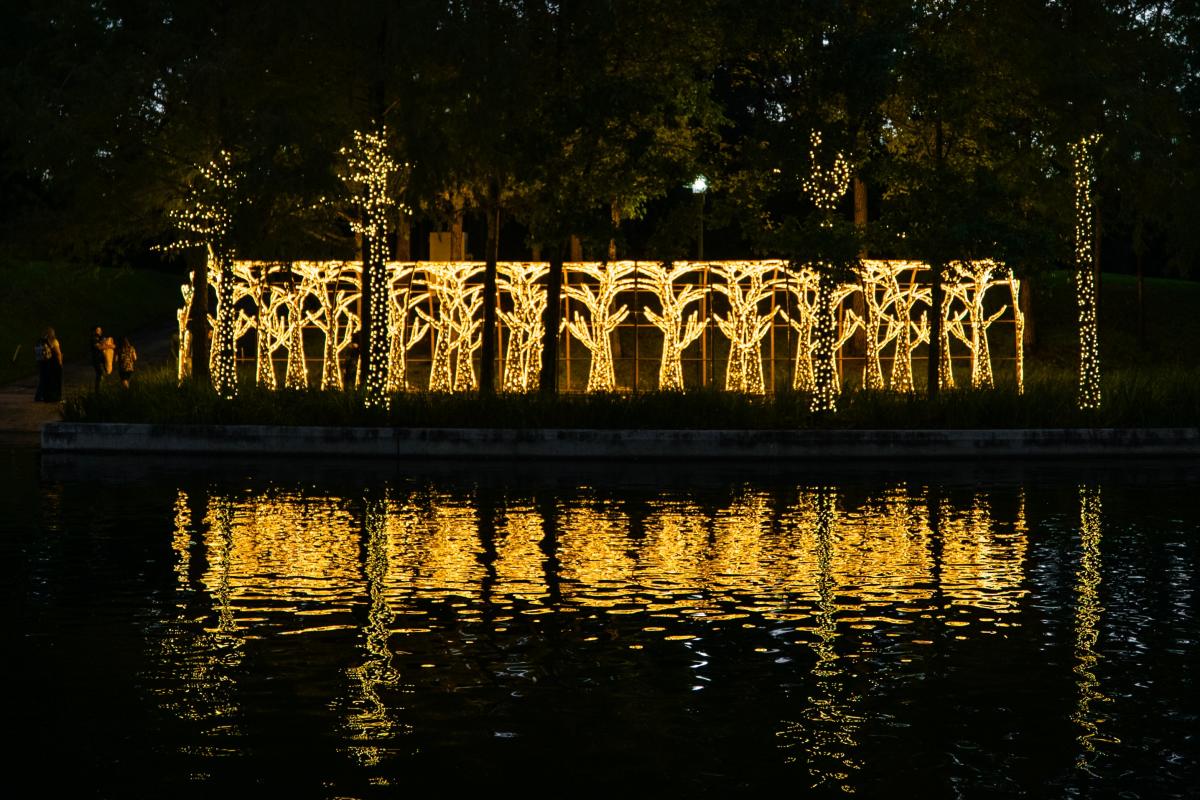 Light displays shaped like trees form a tunnel along The Woodlands Waterway, reflecting with a golden light on the water.