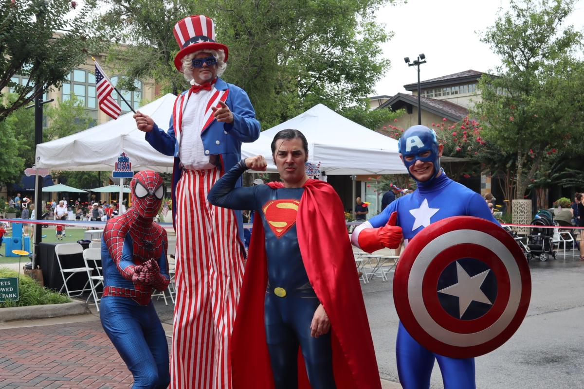 Costumed performers pose for the camera at the 4th of July Parade on Market Street. Among them are Spider-Man (acting as if he were going to shoot webs), Uncle Sam (on stilts, pointing at the camera and waving an American Flag), Superman (from the 2013 film, "Man of Steel," flexing his right arm), and the classic Captain America (offering a thumbs up with the hand not holding his shield).