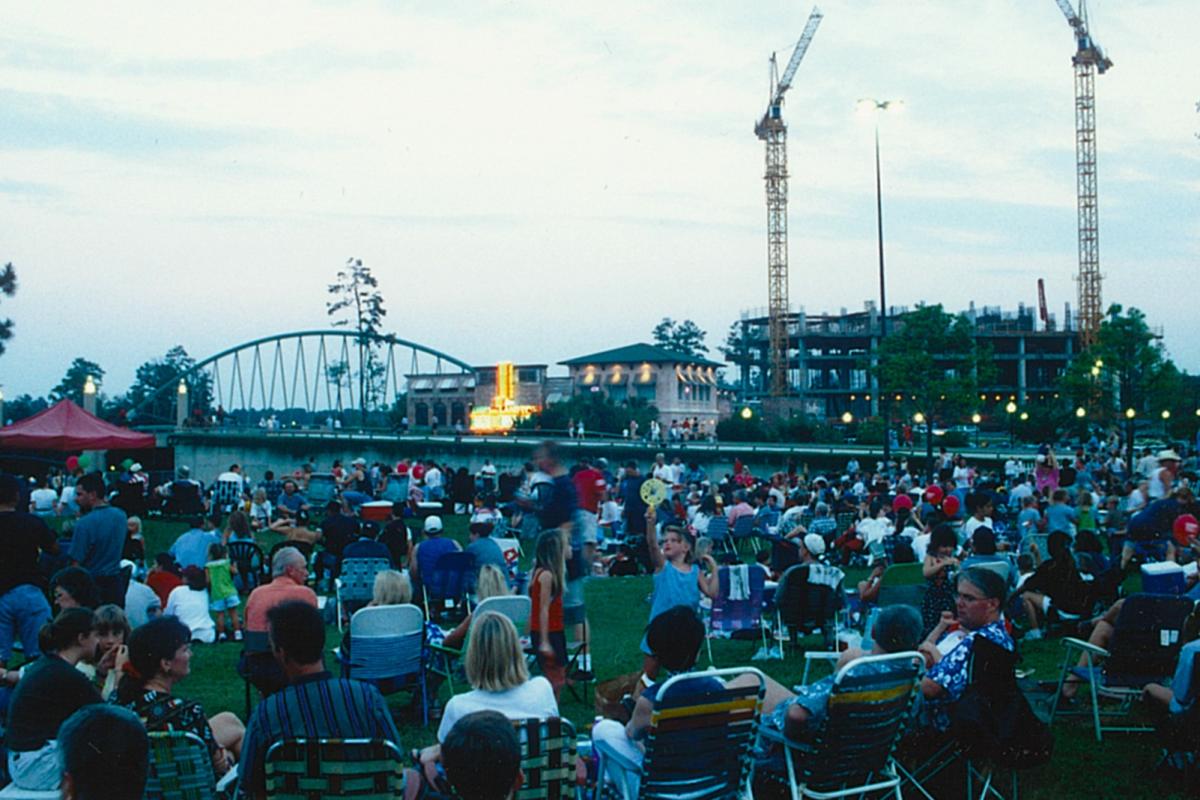 Dozens of spectators gather with lawn chairs in a park beside The Woodlands Mall (where Kirby Ice House sits today) to view the Red, Hot & Blue fireworks on the Fourth of July. Historical photo of RH&B.