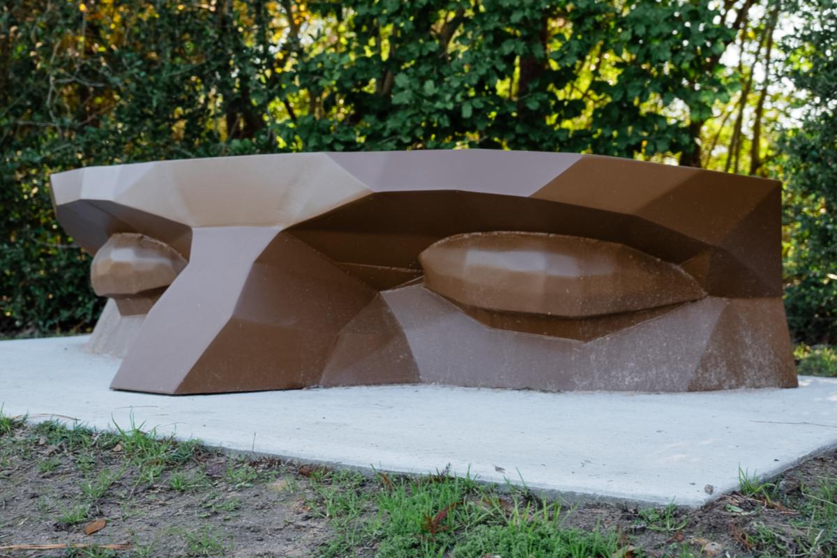 A brown metal park bench shaped like the cross-section of an angular face, from the tops of the eyebrows to the middle of the bridge of its nose.