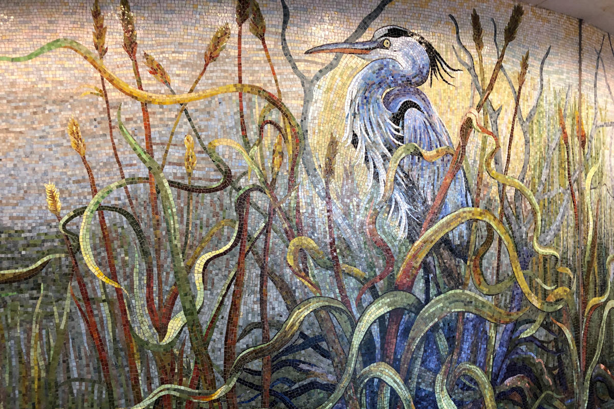 Houston Bayou Mosaic by Dixie Friend Gay. The full art display takes up the entire wall of a long hallways; this section depicts a Great Blue Heron standing among the reeds on a marshy shoreline.
