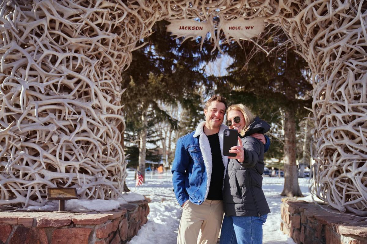 couple taking a photo in front of antler arch in Jackson town square.