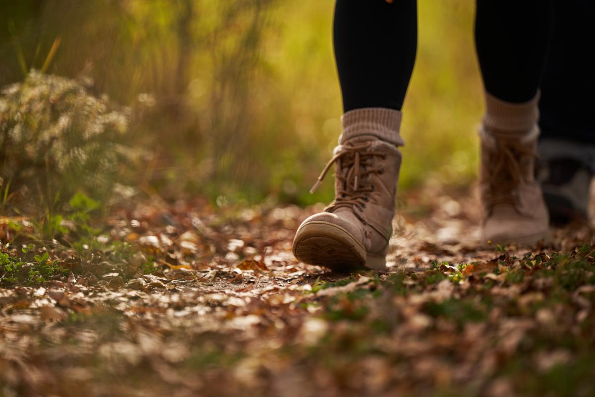 Close-up view of a person wearing lace-up hiking boots and beige socks walking on an autumn leaf-covered trail.