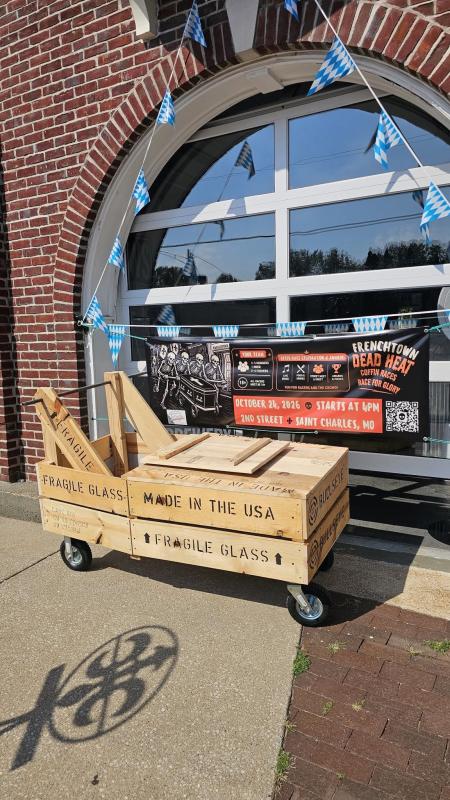 A homemade racing coffin sits outside of Good News Brewing in front of a sign for the Frenchtown Dead Heat Coffin Races.
