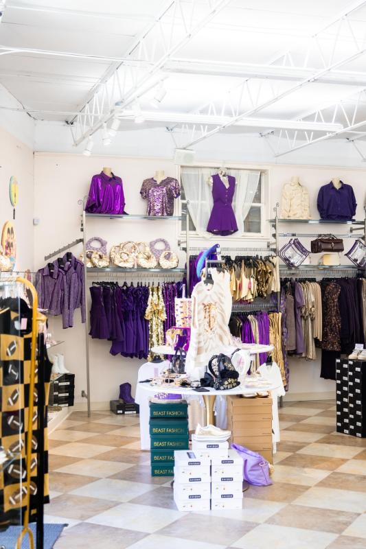 Purple and gold fashion items displayed inside a Baton Rouge boutique, including dresses, tops, jewelry, and accessories.