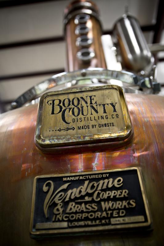 A closeup photo of a copper still. The tags on the still say Boone County Distilling Co. Made by Ghosts and Manufactured by Vendome Copper and Brass Works Inc. Louisville, Kentucky