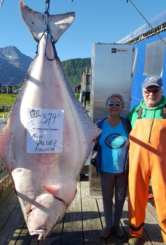 Two people stand next to a very large halibut