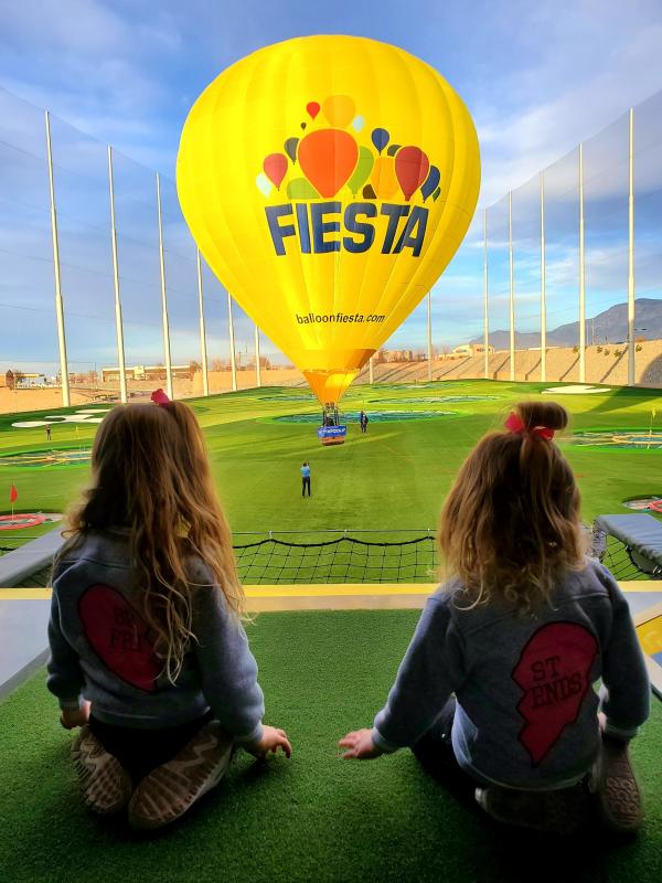 Two little girls look at a hot air balloon that floats above the Topgolf green