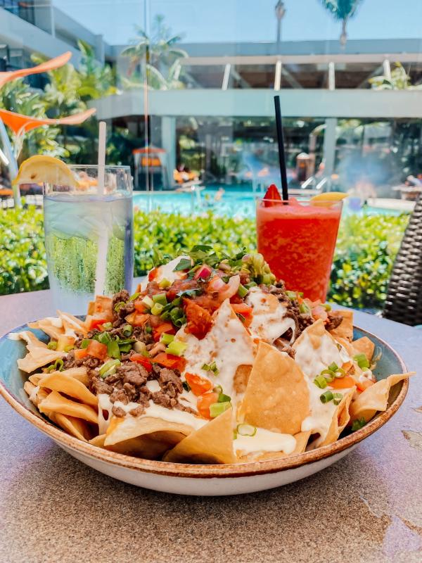 Image of a plate of nachos, glass of water, and a red, strawberry-flavored slushie beverage.