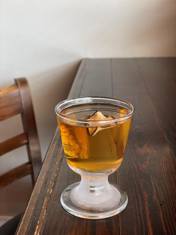 A golden cocktail sits on a wooden table.