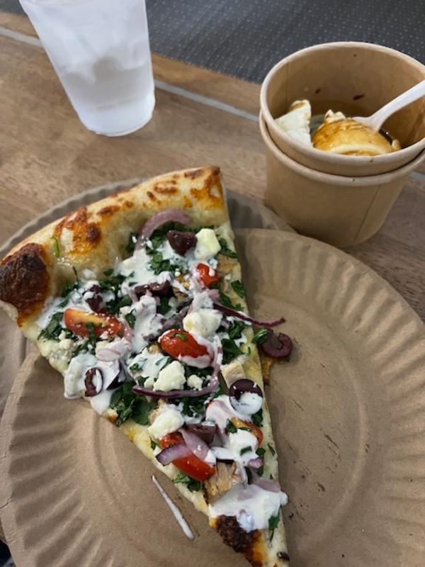 Slice of pizza on a paper plate and cup of dessert on a tabletop at Razzo