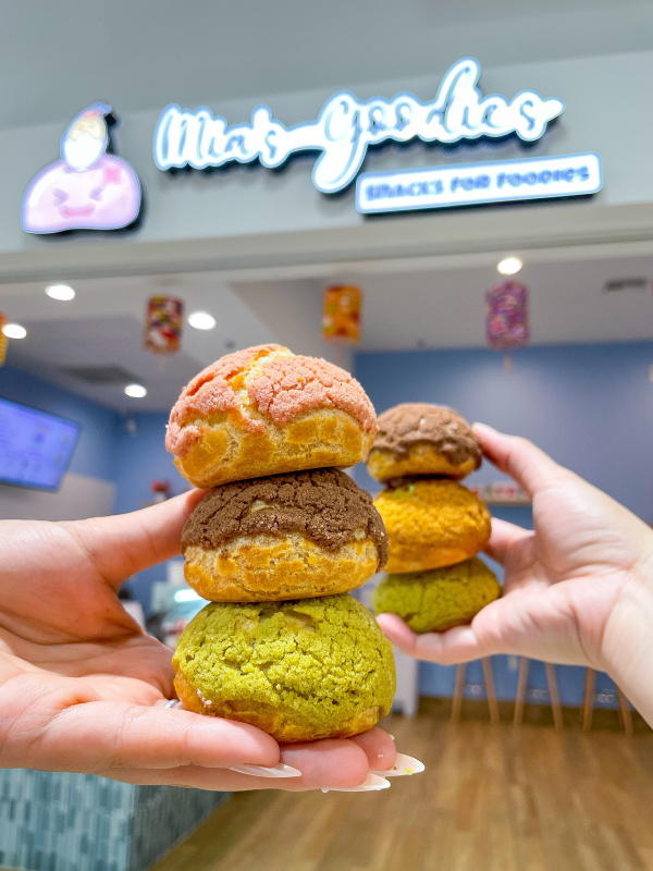 Two hands holding cream puffs at Mia's Goodies