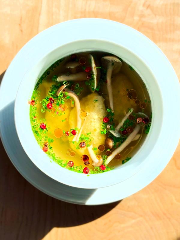 Ricotta Gnudi en Brodo, Beech Mushrooms, Pink Peppercorns, Calabrian Chili Oil, Chive sitting in a while bowl