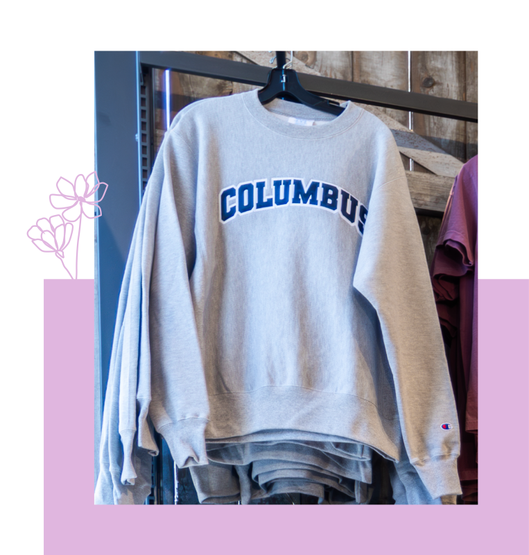 Light gray crewneck sweatshirt with “COLUMBUS” printed across the front in blue block letters, hanging on a clothing rack
