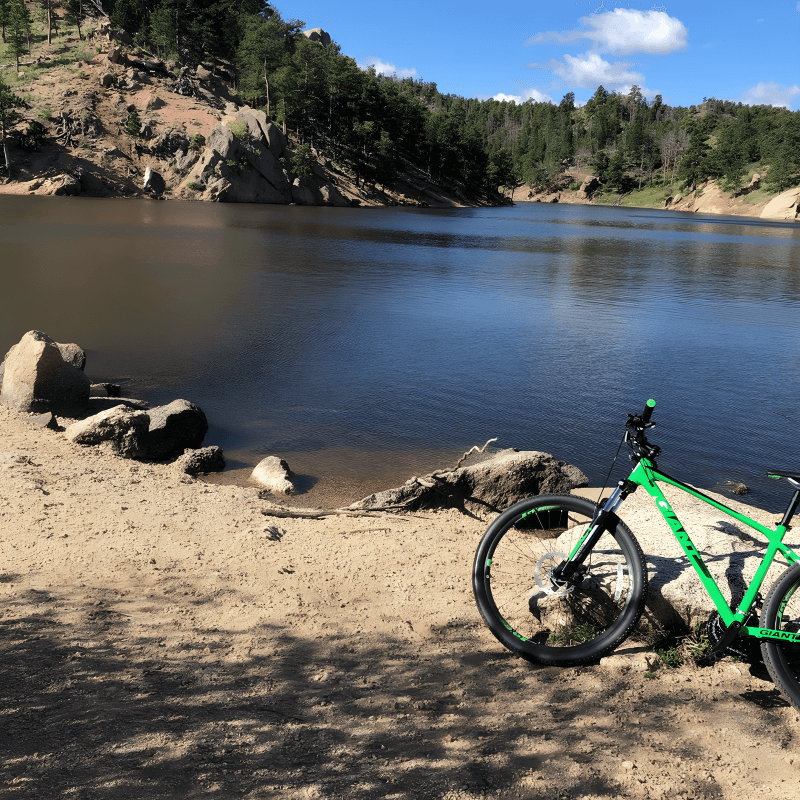 A green bicycle parked next to a lake with Crystal Ridge in the background. The ridge is covered in green trees and shrubs. The sky is blue and cloudless.