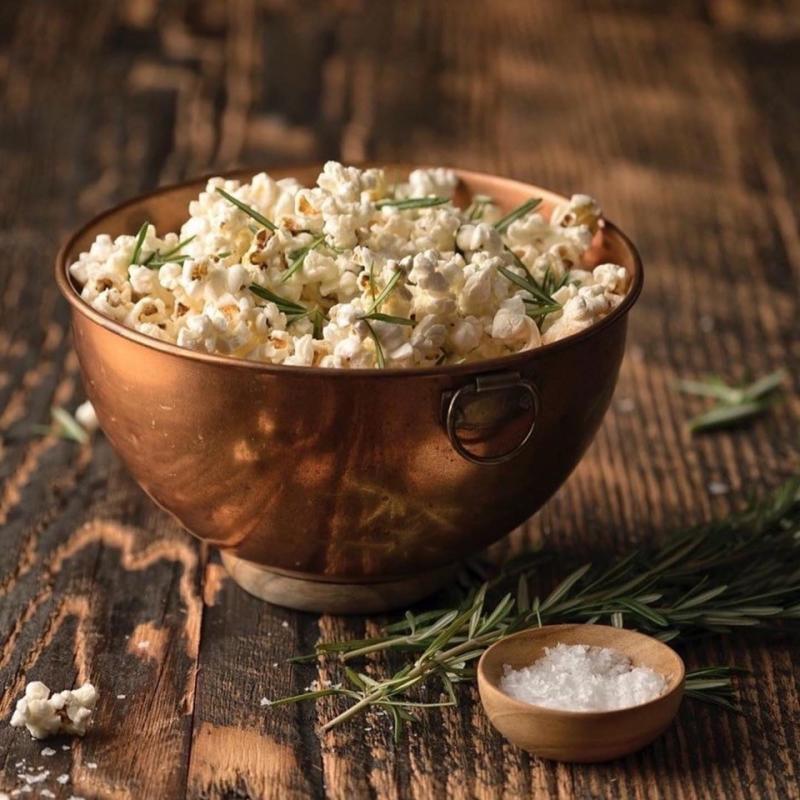 A copper bowl filled with Popcorn sitting on a rustic wooden table at Micro Bar + Bites