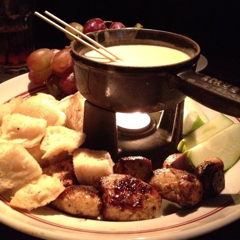 A fondu pot surrounded by bread cubes, sliced green apples, red grapes, and cubed meat from Redstone American Grill