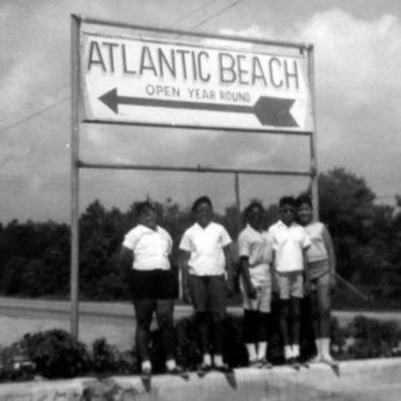 Black and white photo of five children beneath a roadside sign that reads "Atlantic Beach. Open Year-Round" with an arrow pointing left