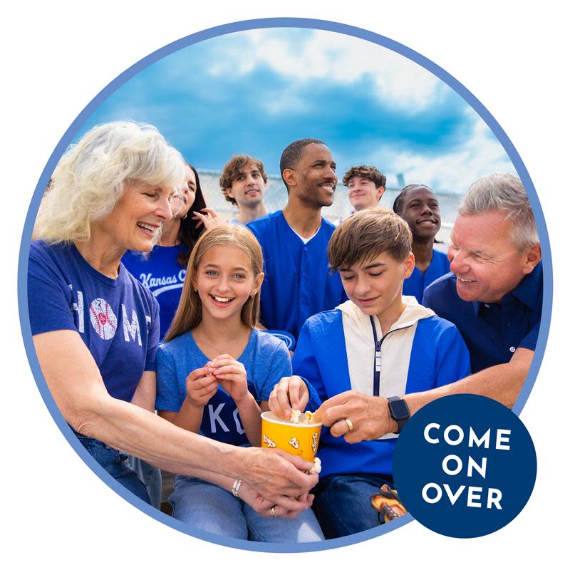 Grandparents with their grandchildren enjoy a Kansas City Royals game from the stands while eating popcorn.