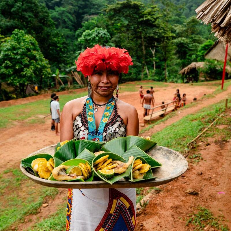 Mulher Emberá-Wounaan oferecendo comida tradicional embrulhada em folhas de bananeira na comunidade