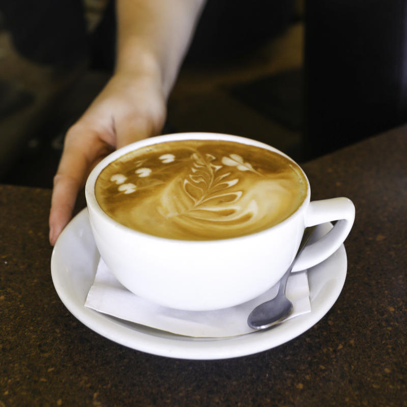 A hot latte in a white mug with a saucer.