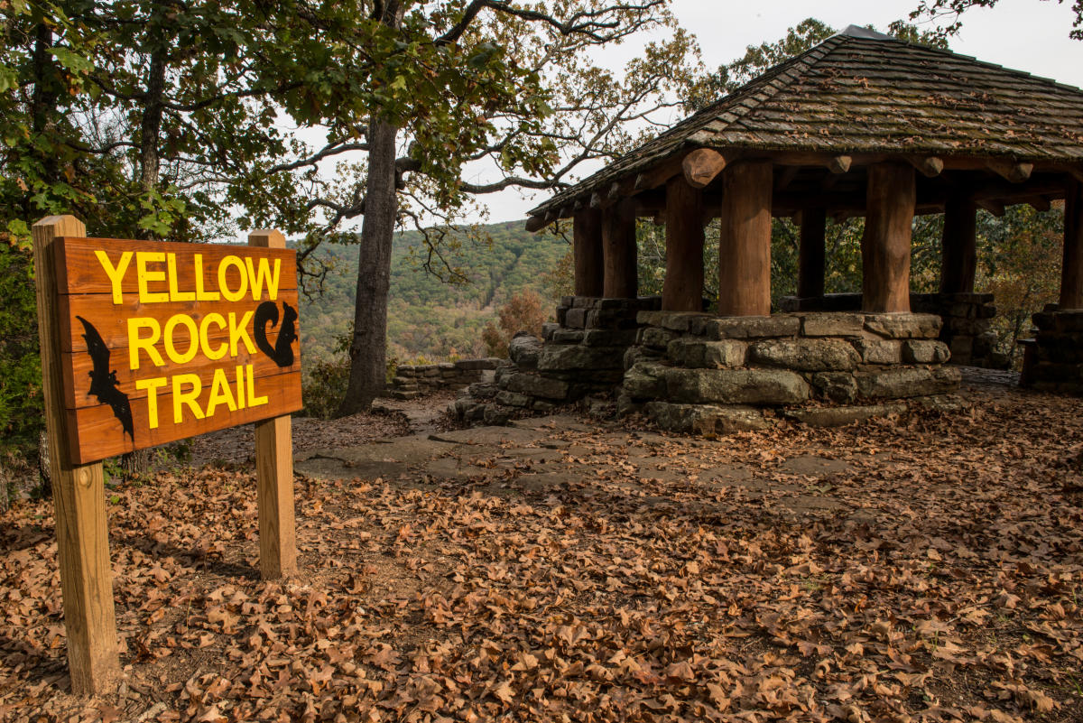 Yellow Rock Trail sign in yellow letters in front of a wood and stone structure at devils den state park.