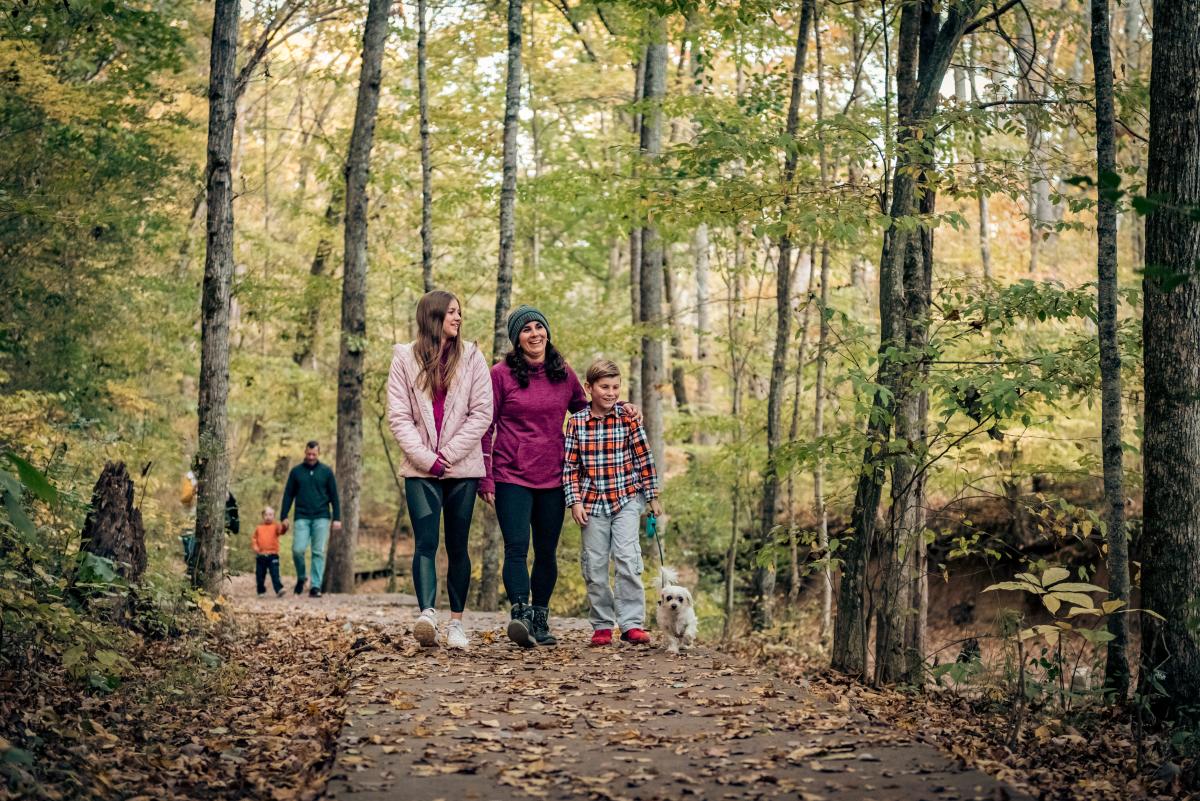 family walking on a paved trail through the woods in the fall