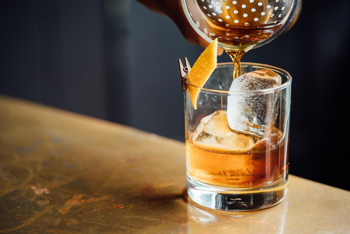 A bartender pouring the rest of an old fashioned in a glass