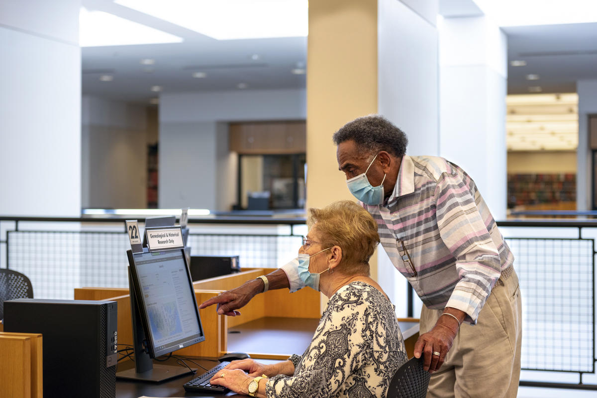 Two adults wearing masks looking at a computer in the Genealogy Center in Fort Wayne, Indiana.